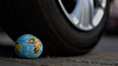Das Foto zur Erklärung "300 Euro für Kinder, 6.000 für Autos" zeigt einen kleinen Spielzeug Globus, der von einem Auto überfahren wird